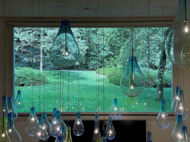 A green sunshine-lit landscape as seen through the window of the Serralves museum's library, with huge decorative lightbulbs hanging from the ceiling